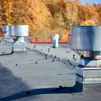 Air roof exhaust ventilation fan system of industrial large commercial building with hooded chimneys flues and ducts in row on roof top selective focus, with lightning protection system.